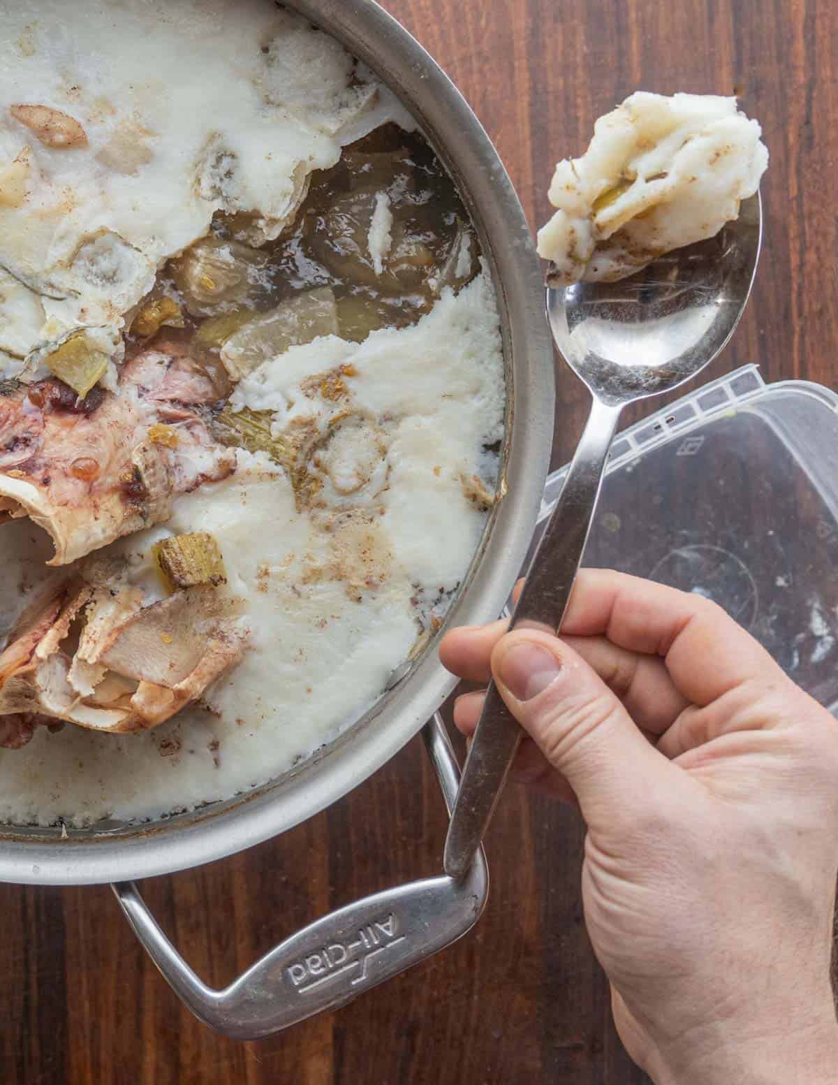 Removing pork fat from the top of a cooked pot of headcheese using a Kunz spoon. 