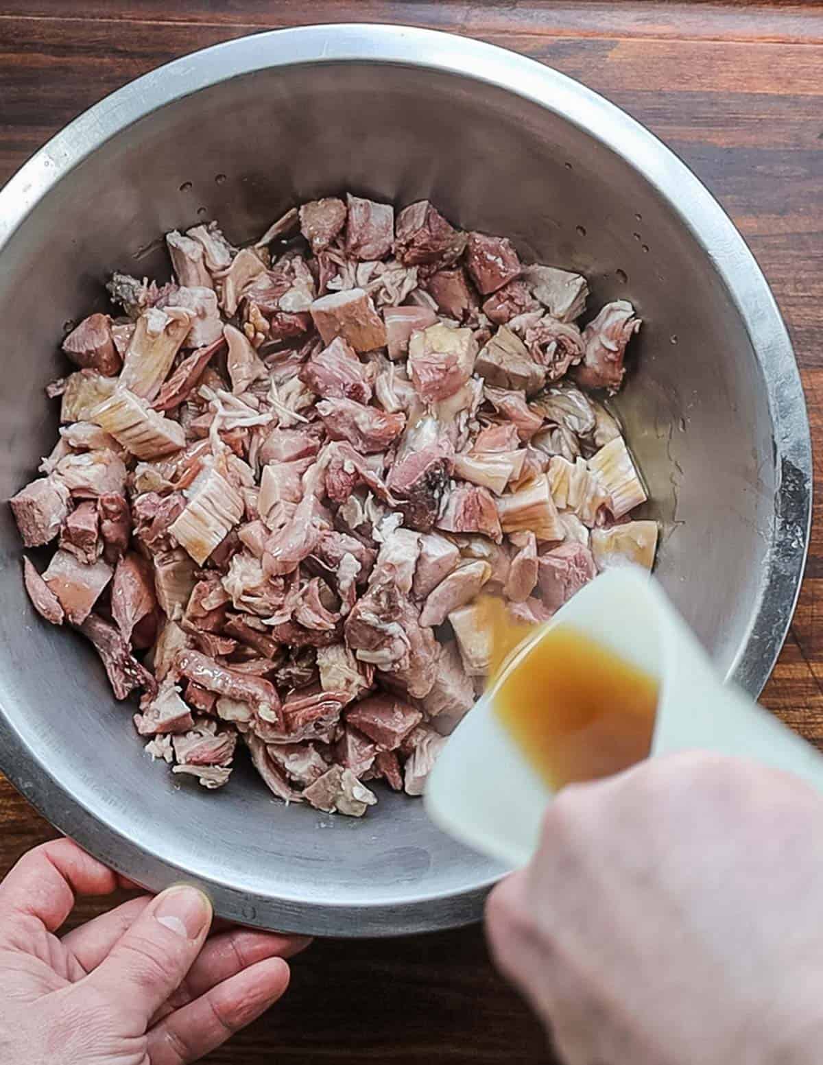 Mixing reduced cooking liquid into cooked pork meat in a bowl. 