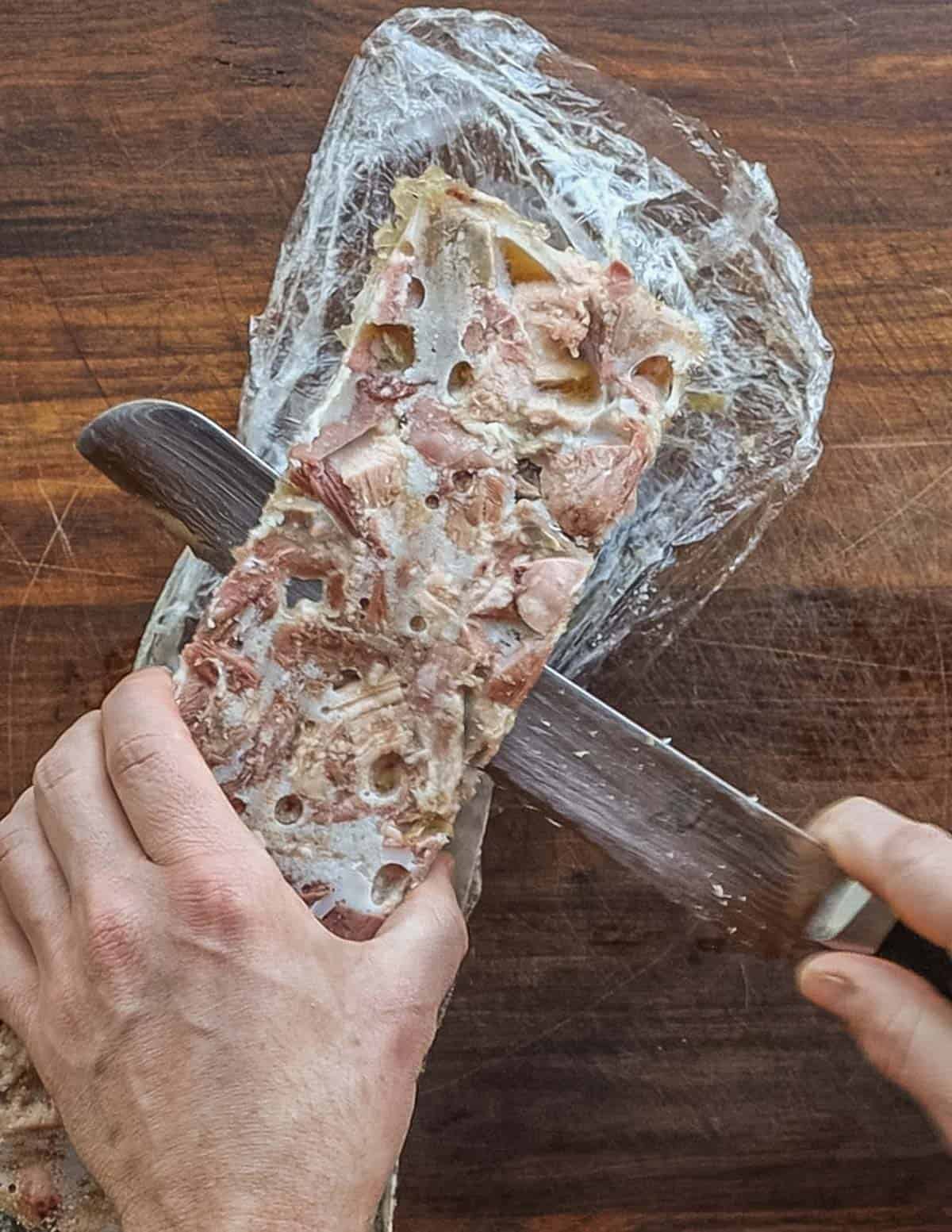 A knife slicing through the top of a loaf of pork headcheese removing fat. 