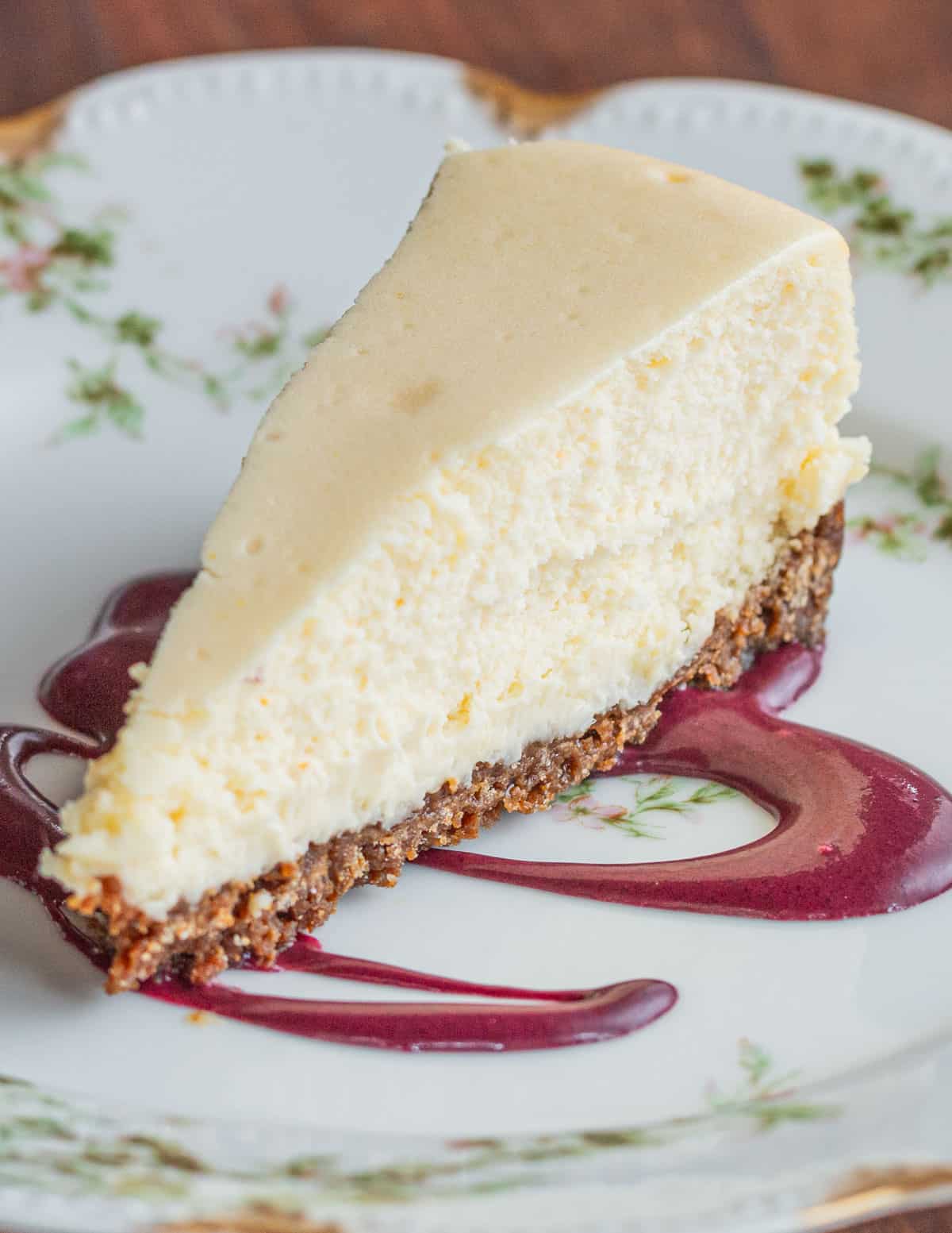 A slice of cheesecake served with a drizzle of purple blueberry coulis sauce. 