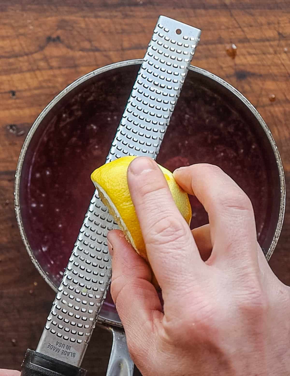 Grating lemon zest and juice into a pot of finished  blueberry sauce. 