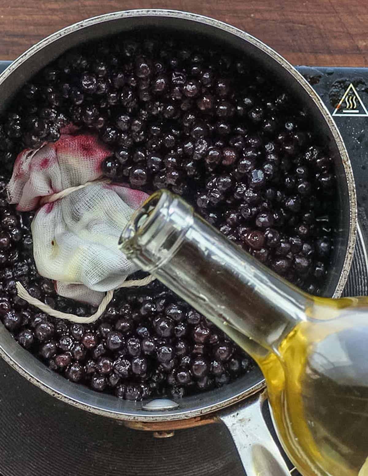 Adding white wine to a pan of blueberries. 