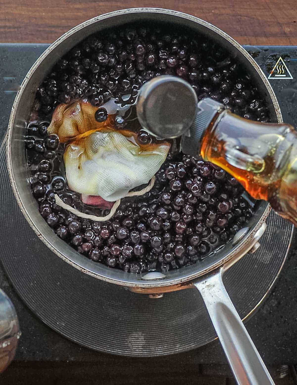 Adding maple syrup to a pan of blueberries. 