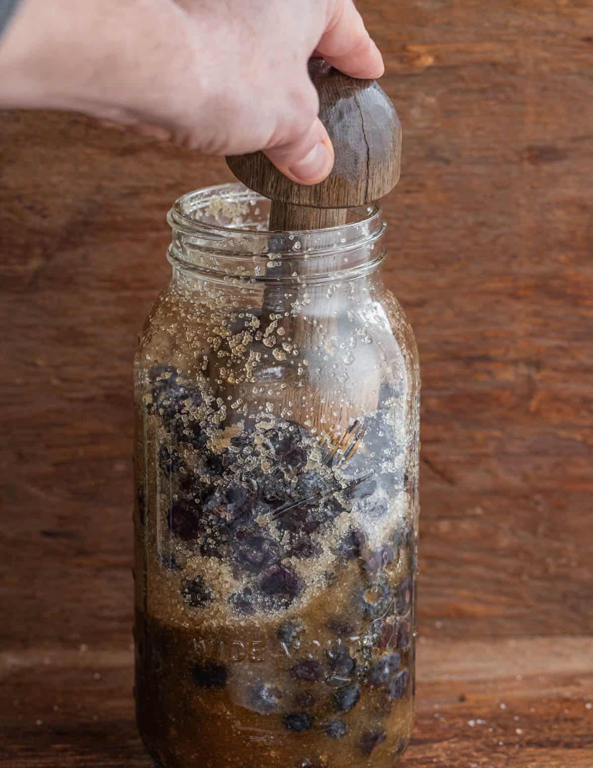 Crushing blueberries in a jar using a mallet.