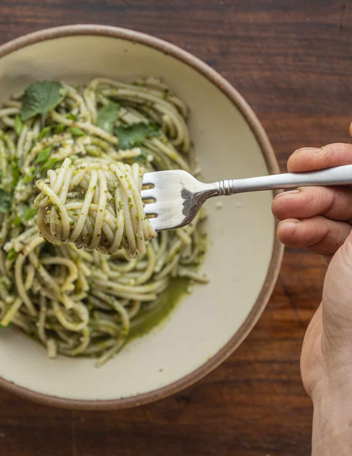 Twirling noodles with pesto using a fork. 
