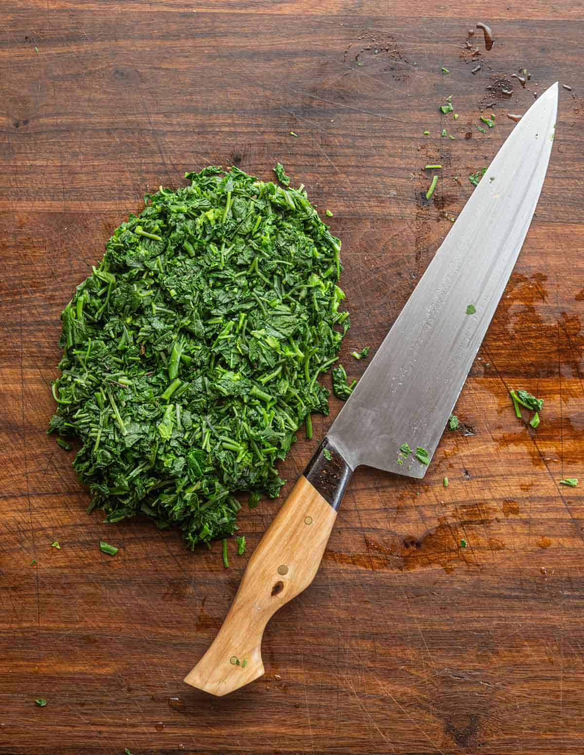 Finely chopped garlic mustard greens on a cutting board next to a chef knife. 