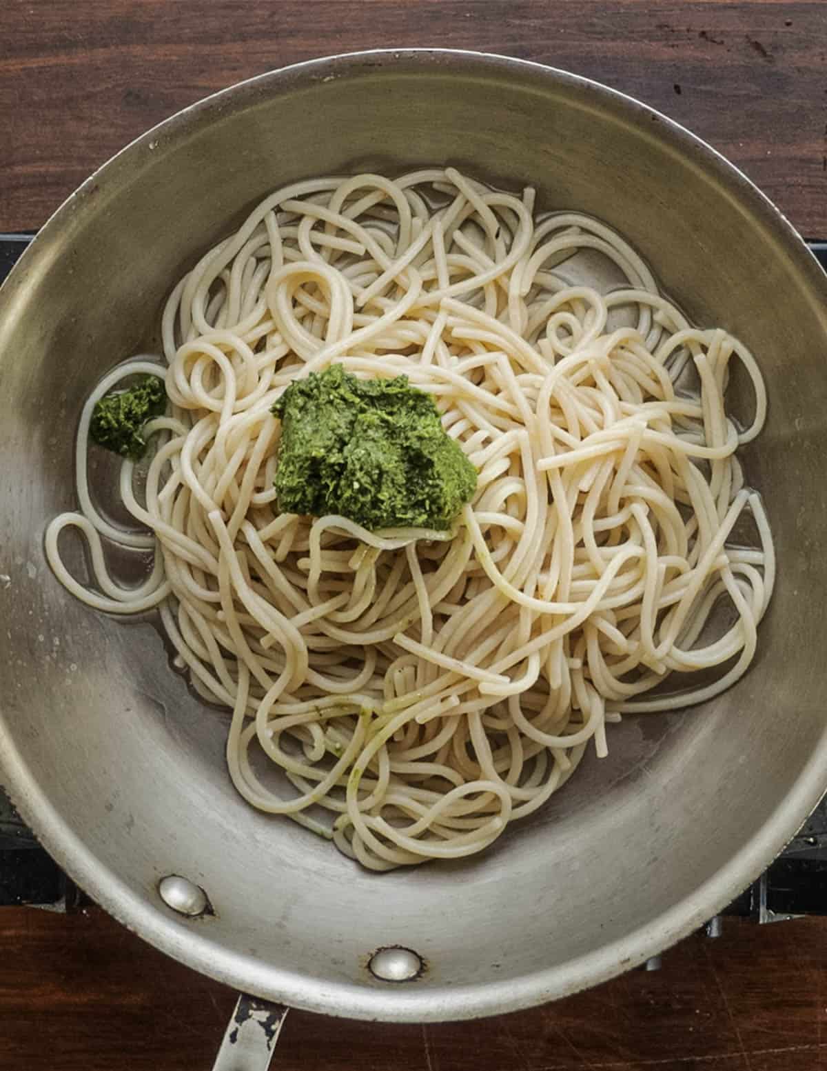 Adding garlic mustard pesto to cooked spaghetti in a pan. 