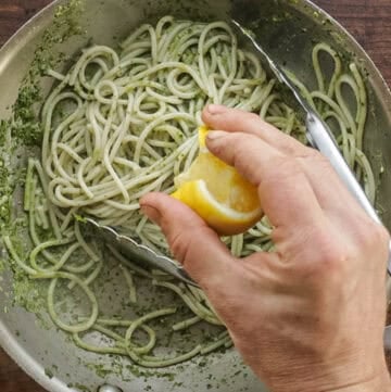 Adding a squeeze of lemon juice to a bowl of pesto pasta.