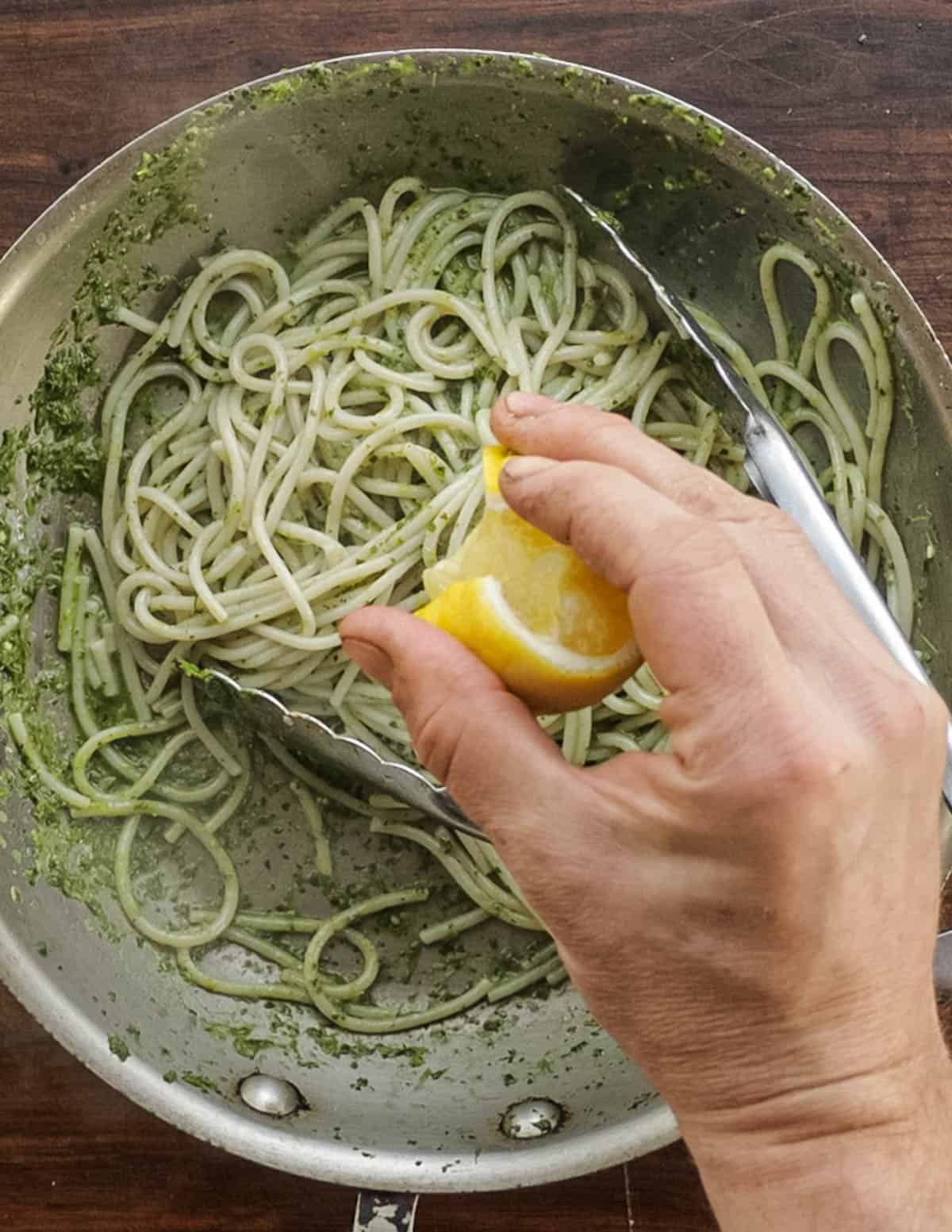 Adding a squeeze of lemon juice to a bowl of pesto pasta. 