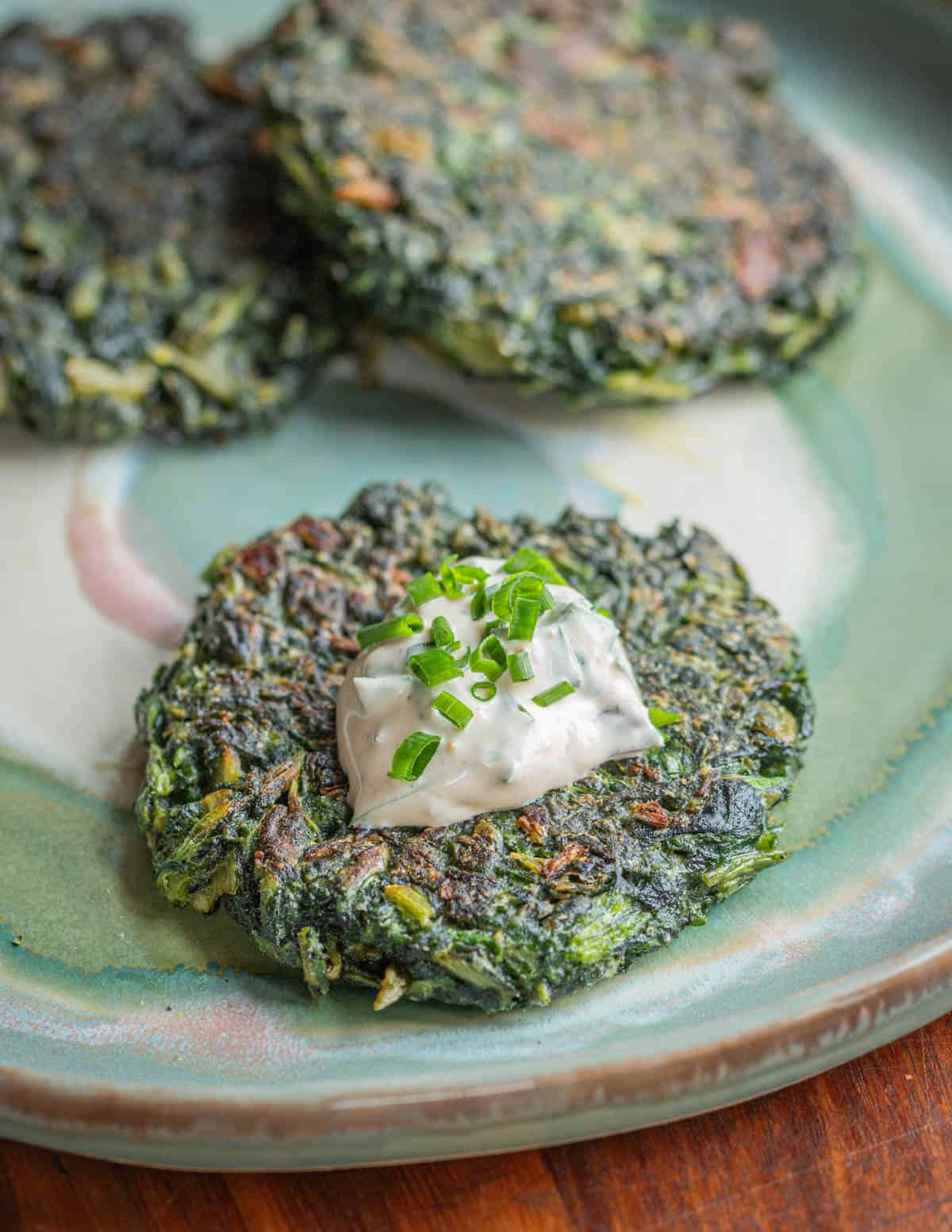Homemade plant based green burgers or spinach patties on a plate with dip garnished with chives. 
