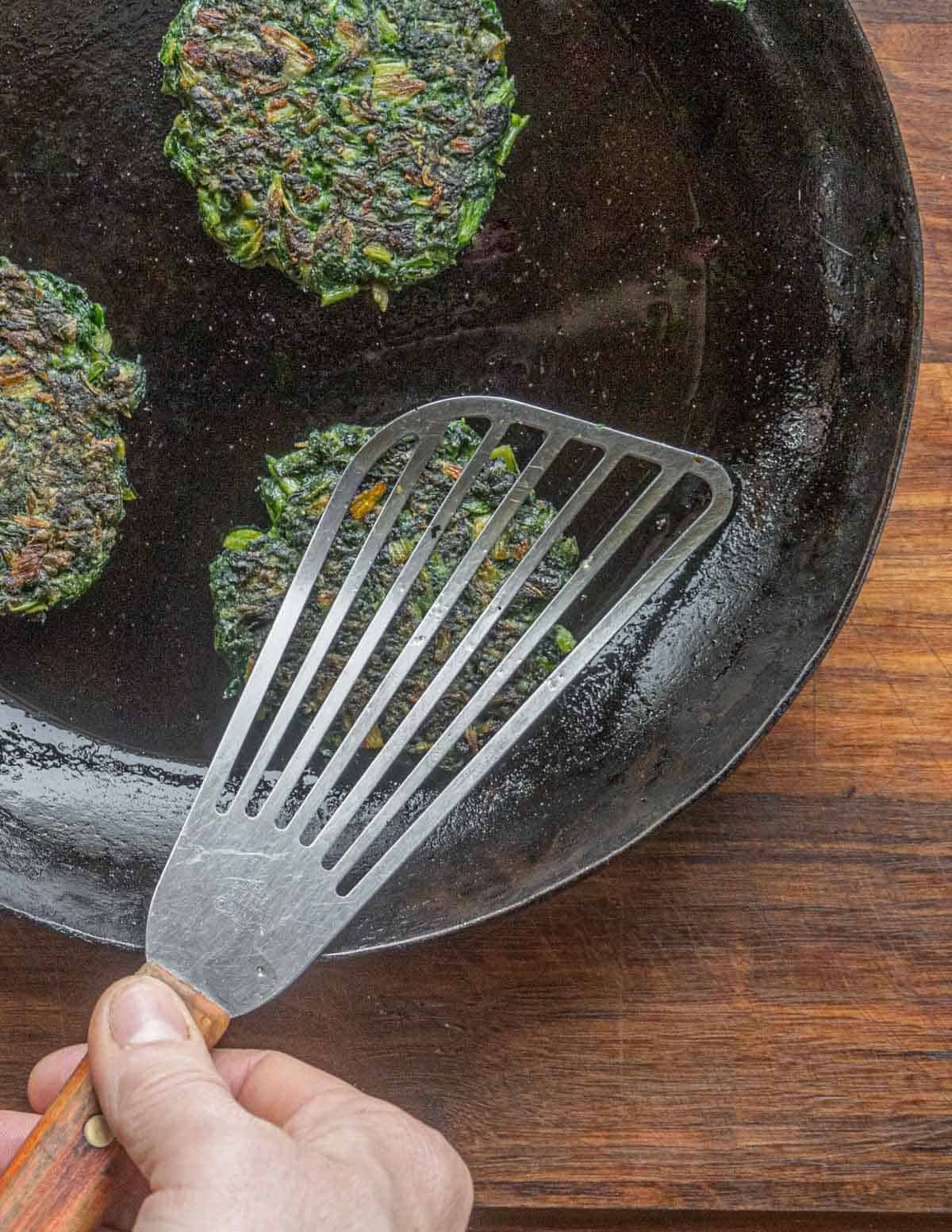 Pressing down on green burgers or spinach patties in a pan.