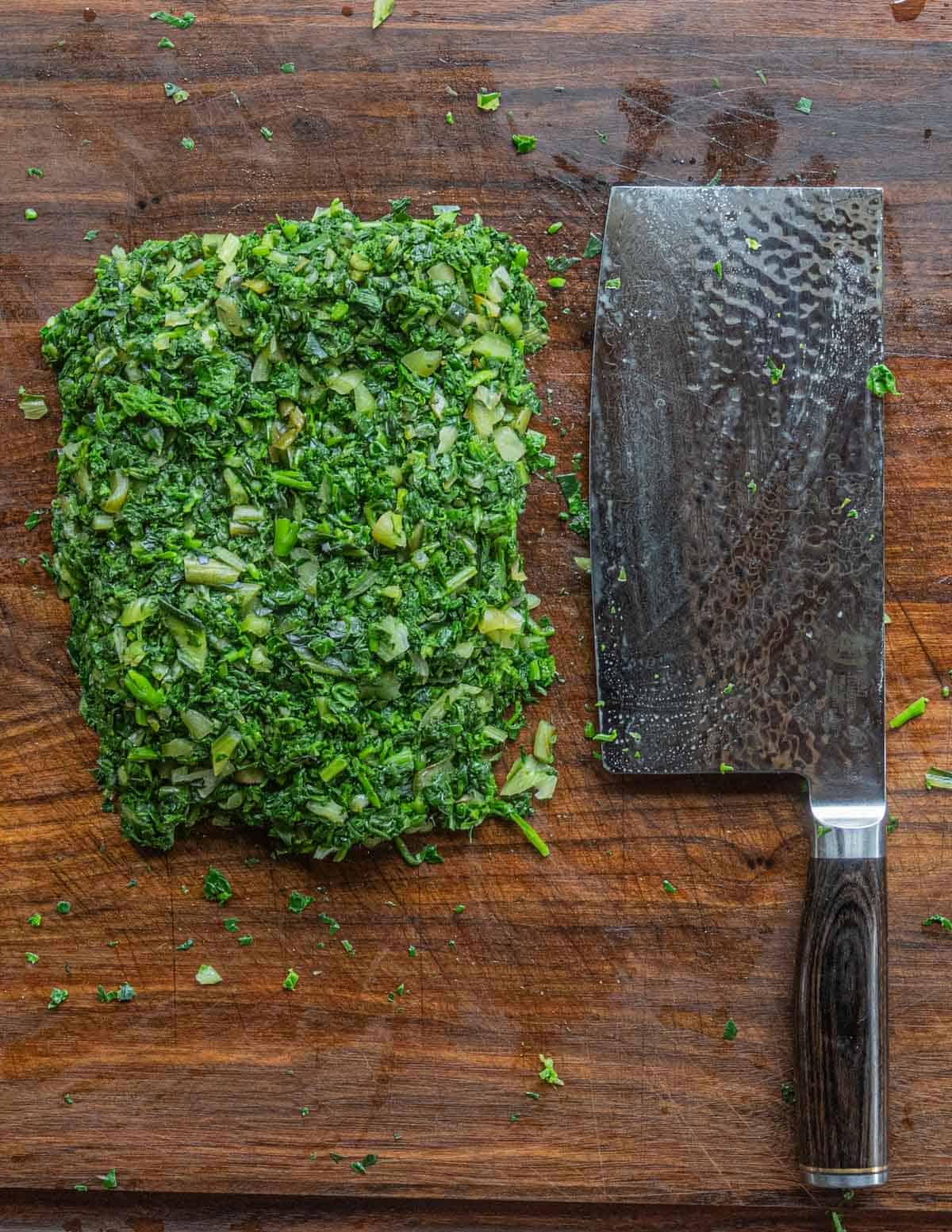 Finely chopped greens next to a chefs knife on a cutting board. 