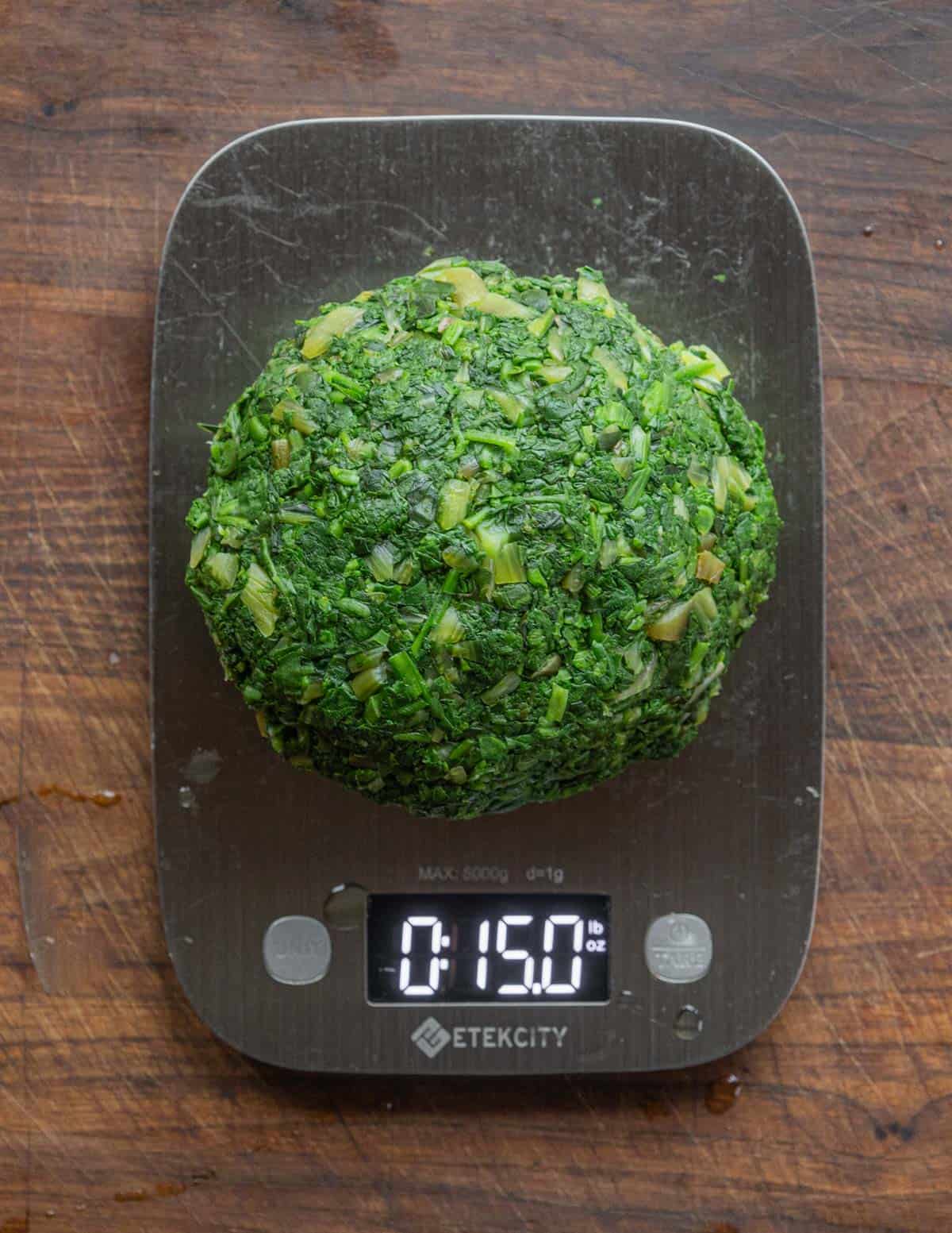 A pile of cooked spinach and leafy greens being weighed on a scale. 
