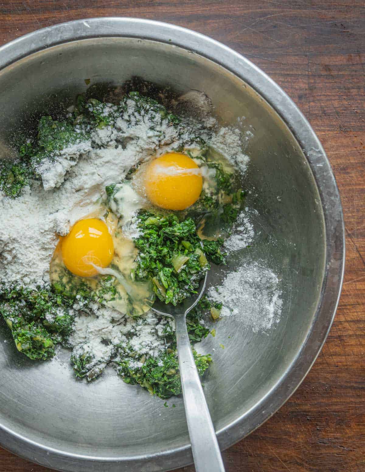 Mixing cooked greens with egg, flour and spices in a bowl. 