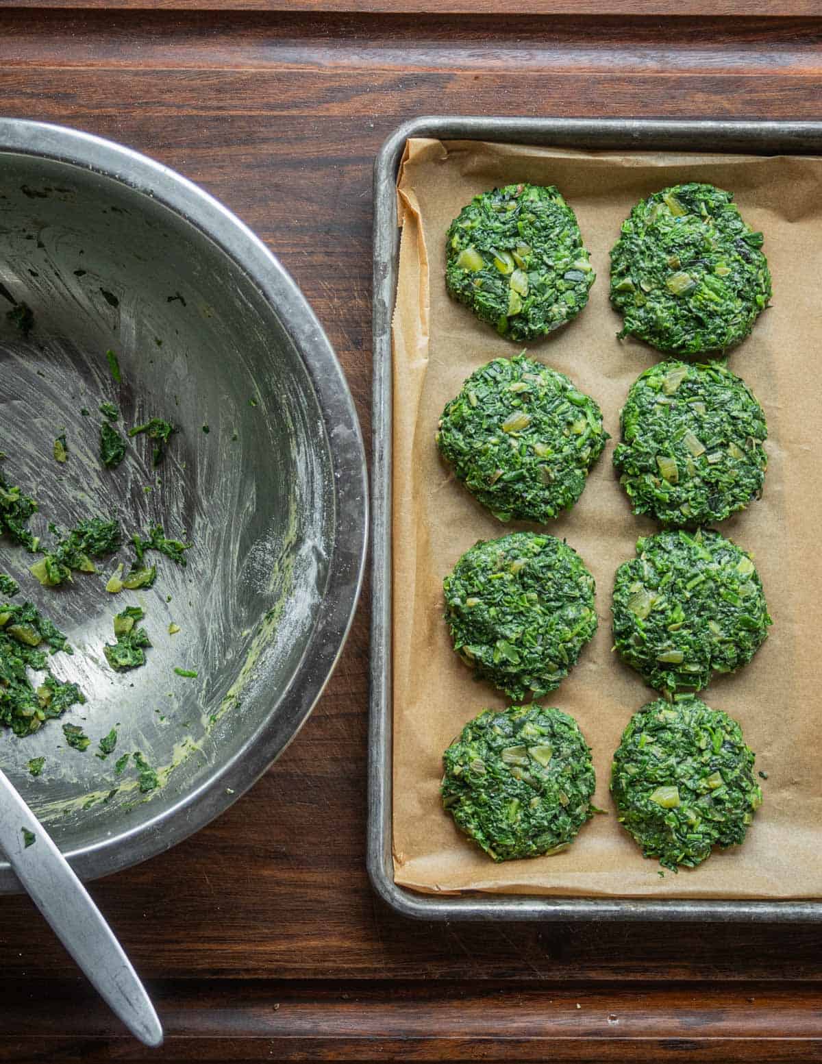 A baking sheet lined with portioned green burgers or spinach patties. 