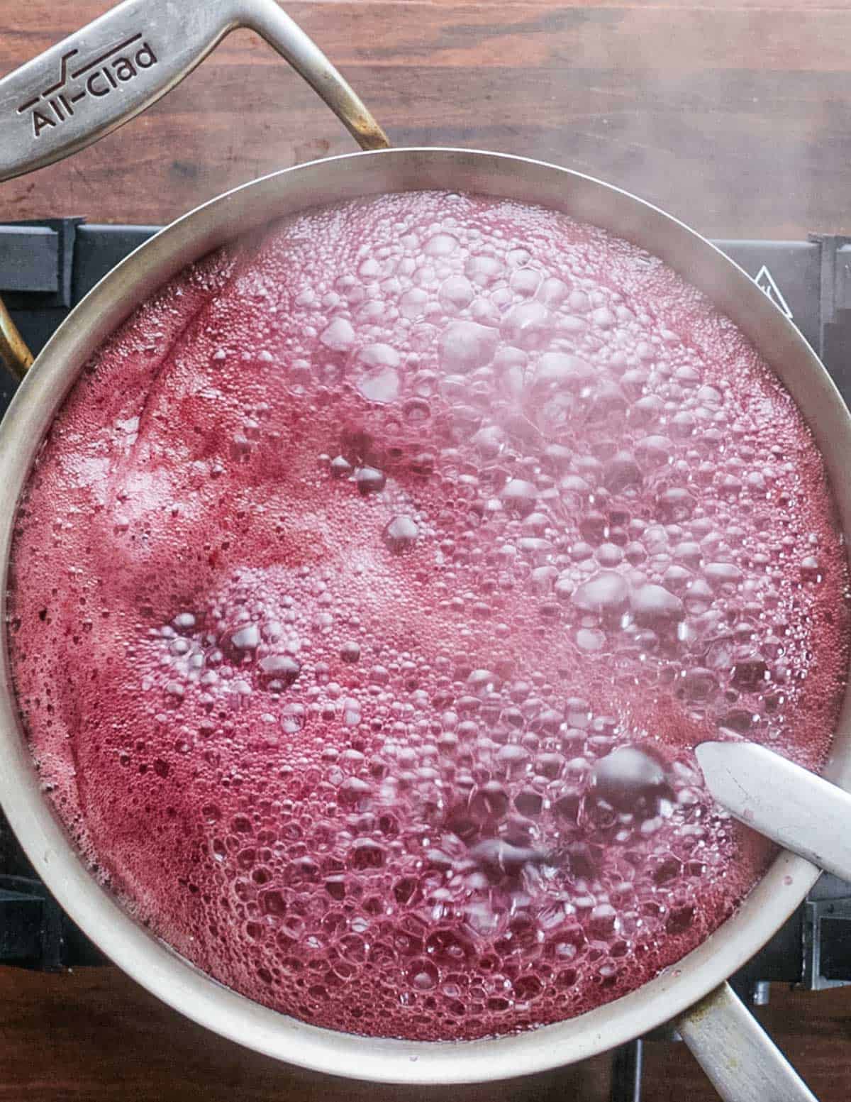 A pot of blueberry syrup cooking showing purple foam.