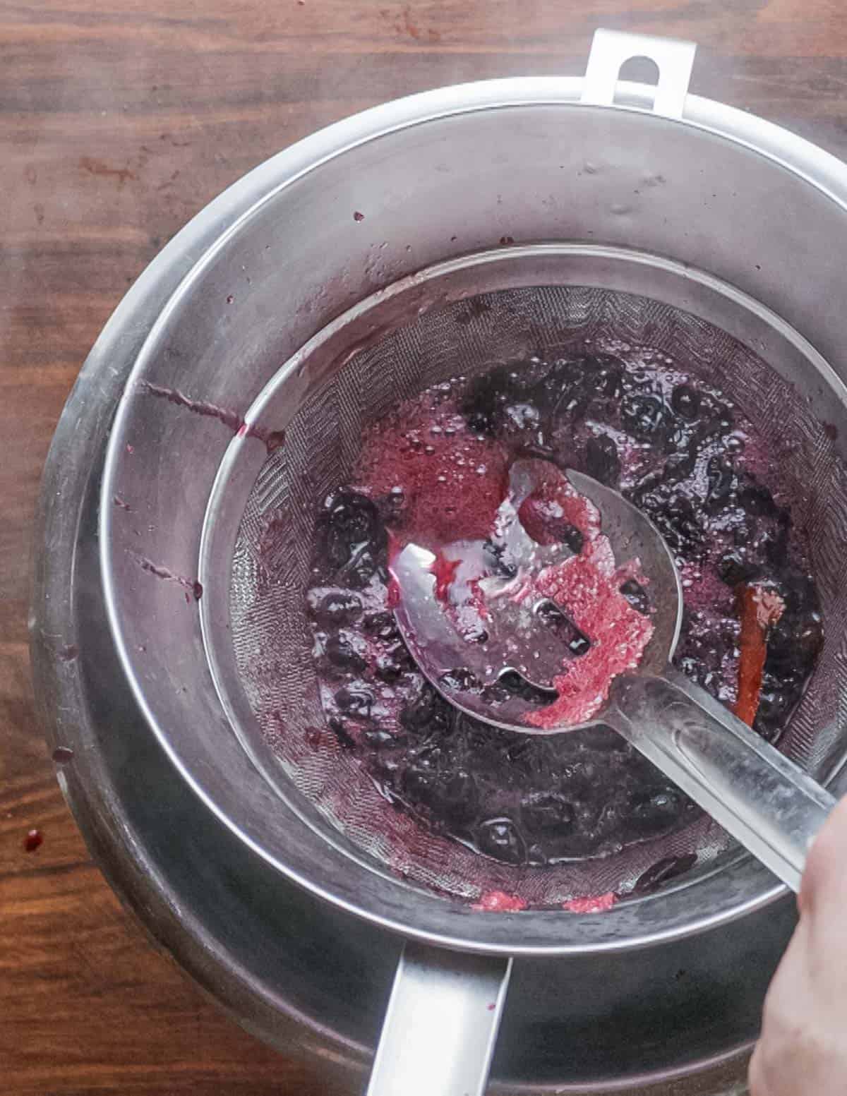 Straining blueberry syrup with a chinois strainer.