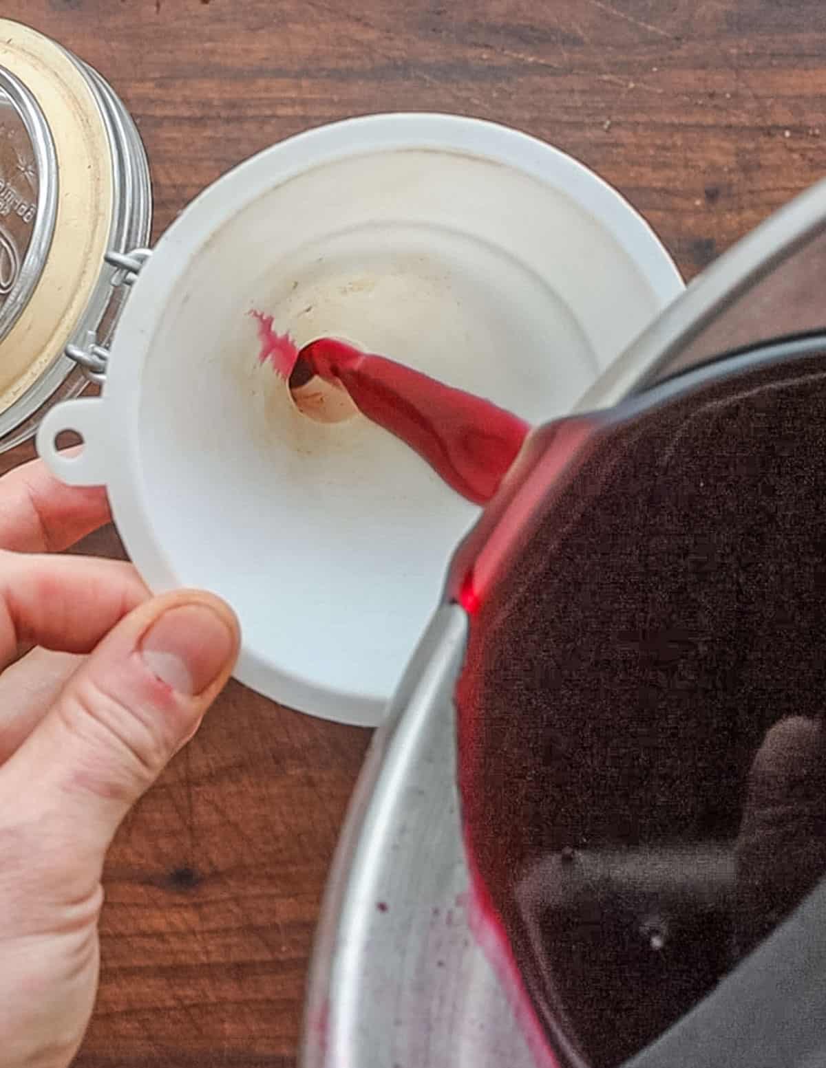 Pouring blueberry syrup into a jar using a funnel.