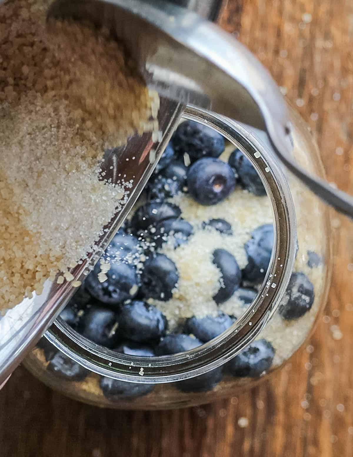 Mixing blueberries and turbinado sugar in a jar to ferment.