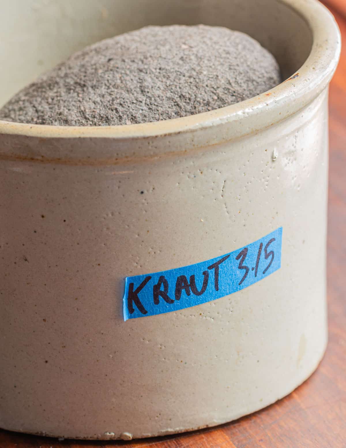 A fermentation crock filled with sauerkraut showing a label and date. 