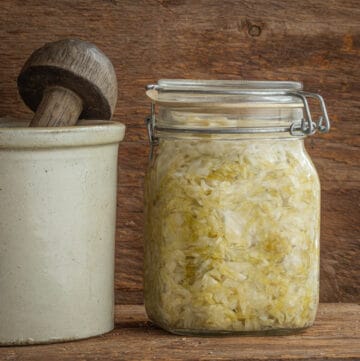 A mason jar filled with sauerkraut next to a ceramic german fermenting crock.