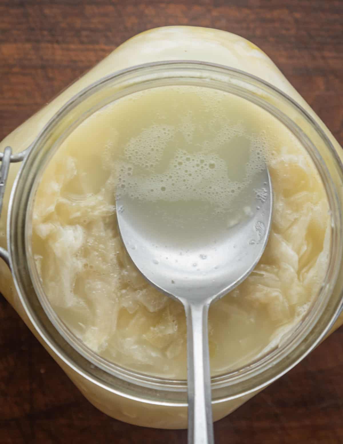 Pressing down on sauerkraut in a jar with a spoon showing brine covering the cabbage.