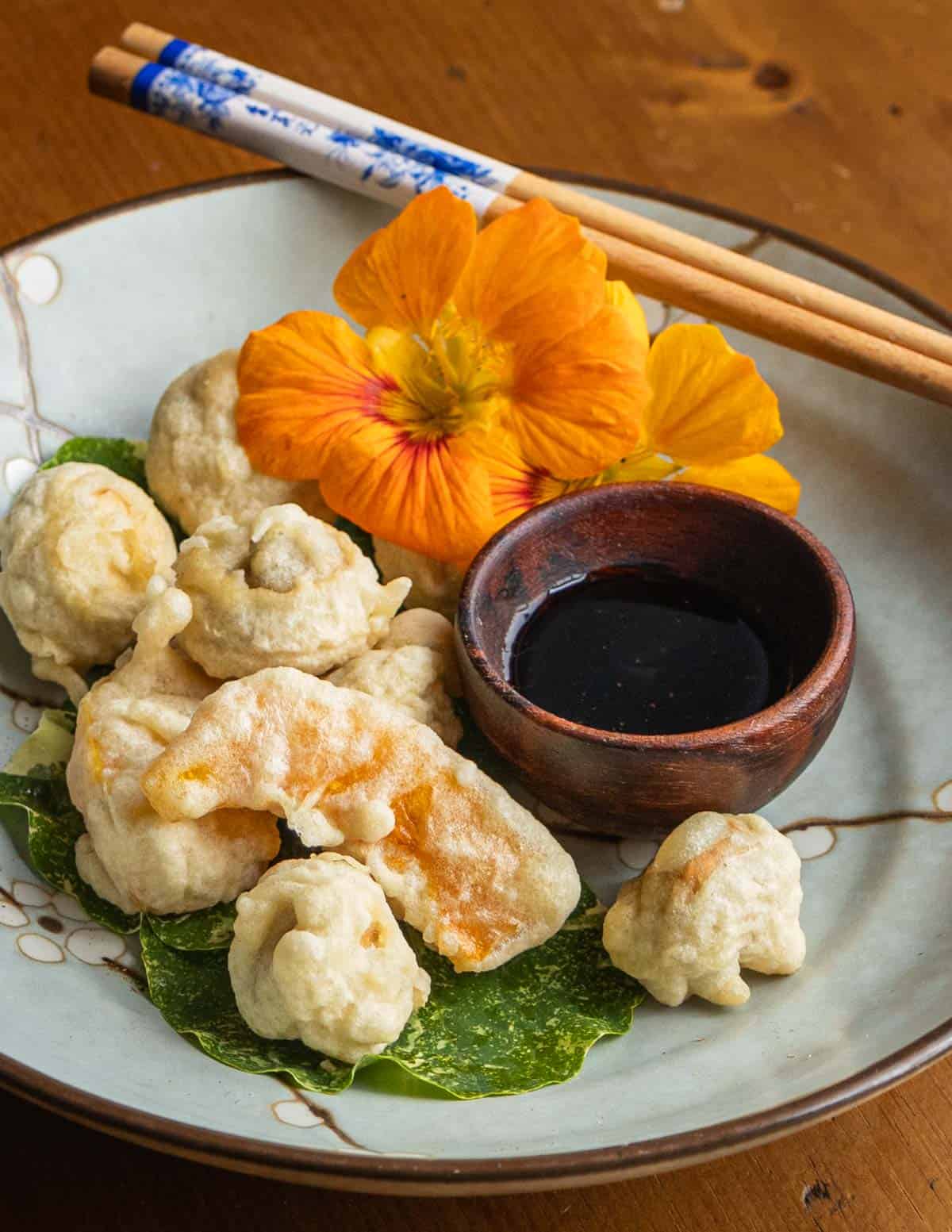 Tempura puffball mushrooms and kabocha squash on a plate next to a dipping sauce in a bowl with a plate garnished with nasturtium leaves. 