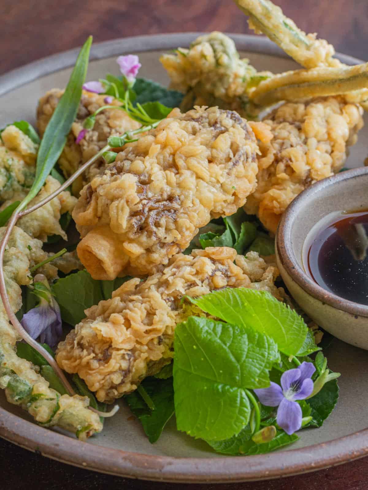 Morel mushroom tempura with basswood leaves, ramp soy dipping sauce and fried fiddleheads on a plate ready to eat. 