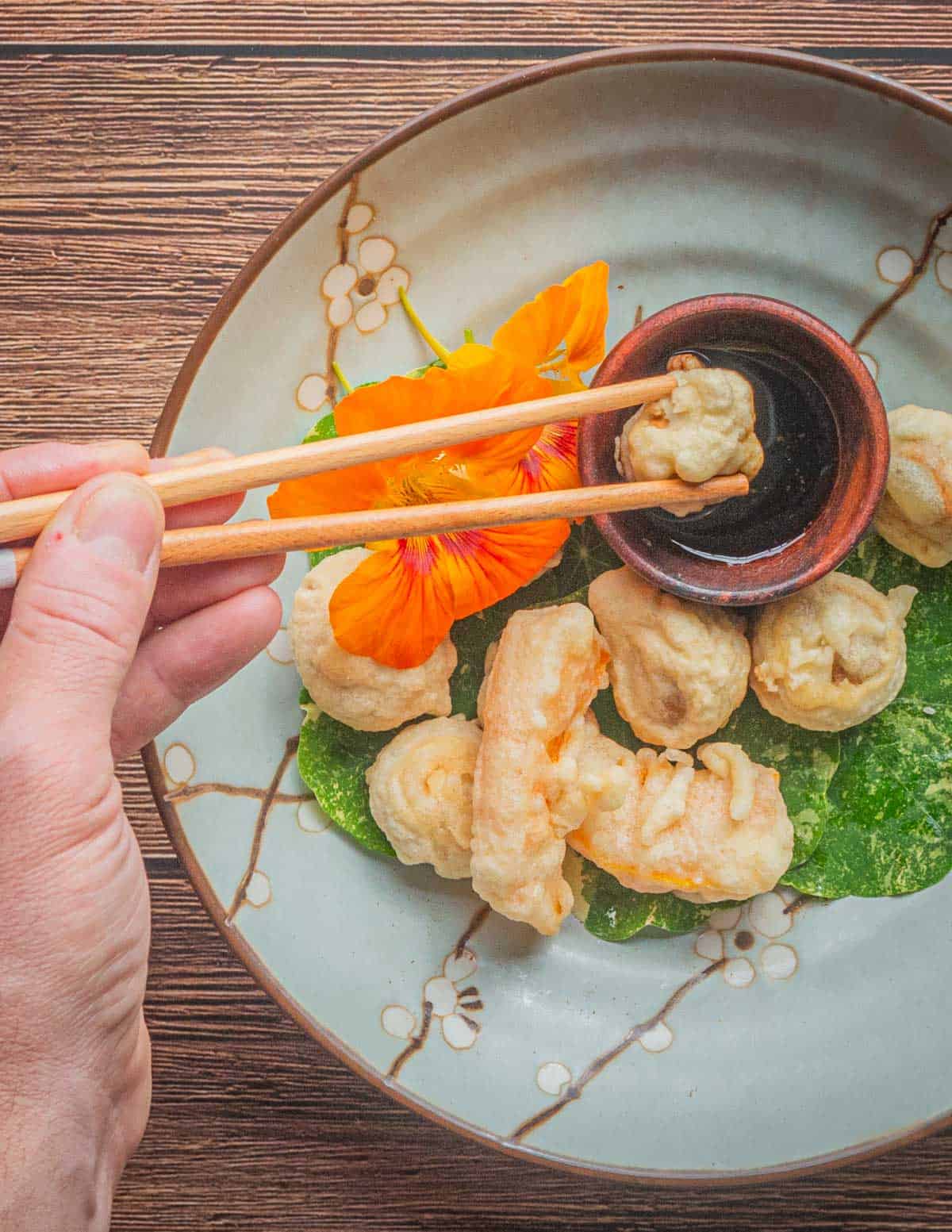 Dipping mushroom tempura into dipping sauce with chopsticks.