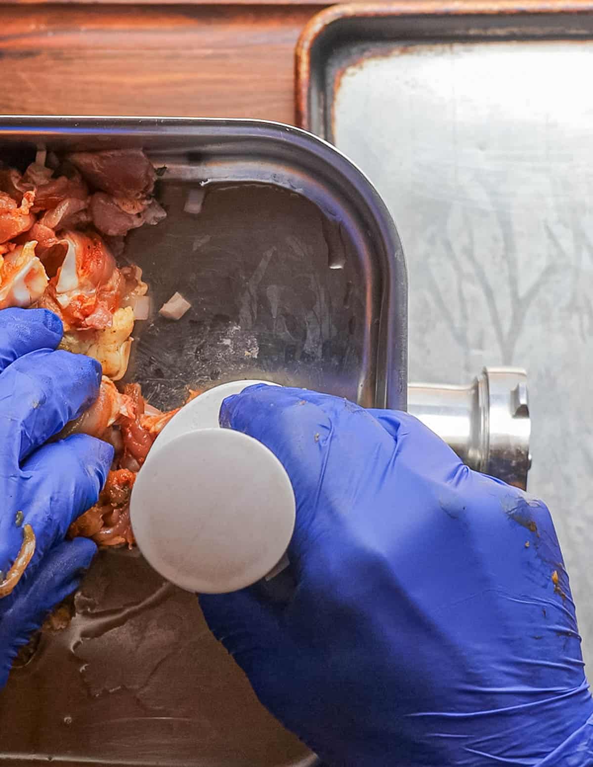 Grinding chicken sausage through a meat grinder. 