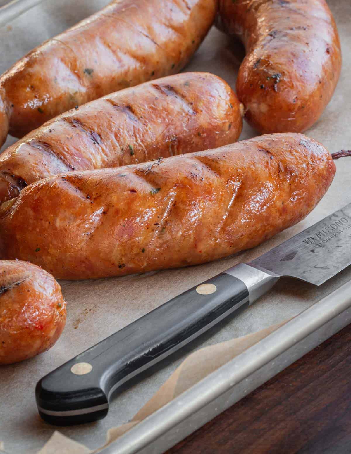 Red smoked chicken andouille sausages on a tray next to a knife. 