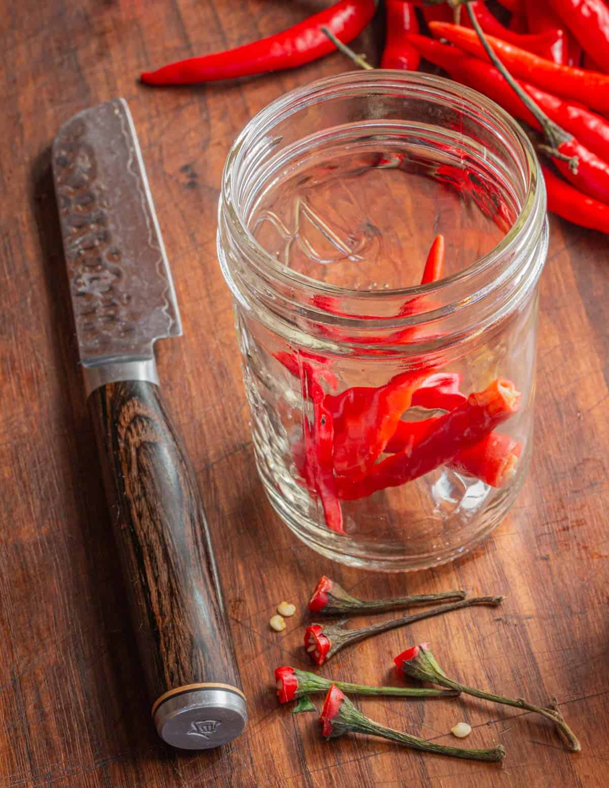 Cutting the stems from hot peppers and putting them in a jar. 