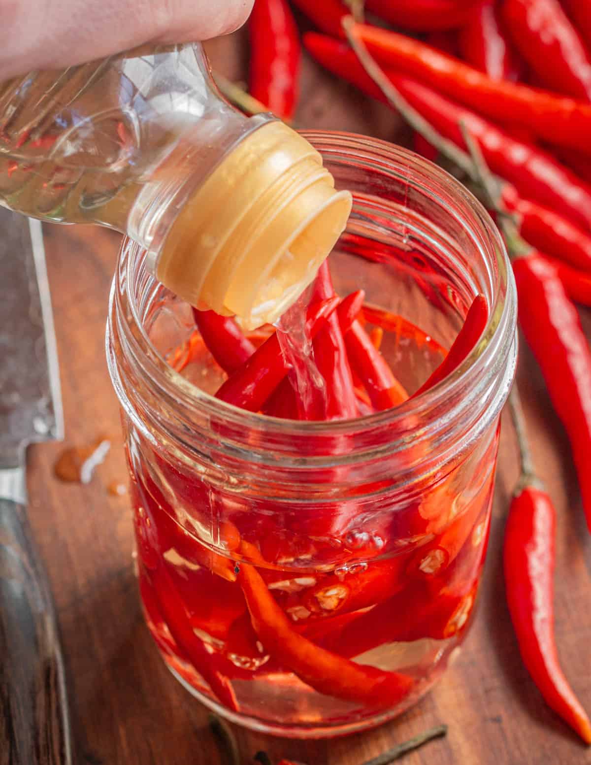 Pouring vinegar over hot peppers in a jar. 