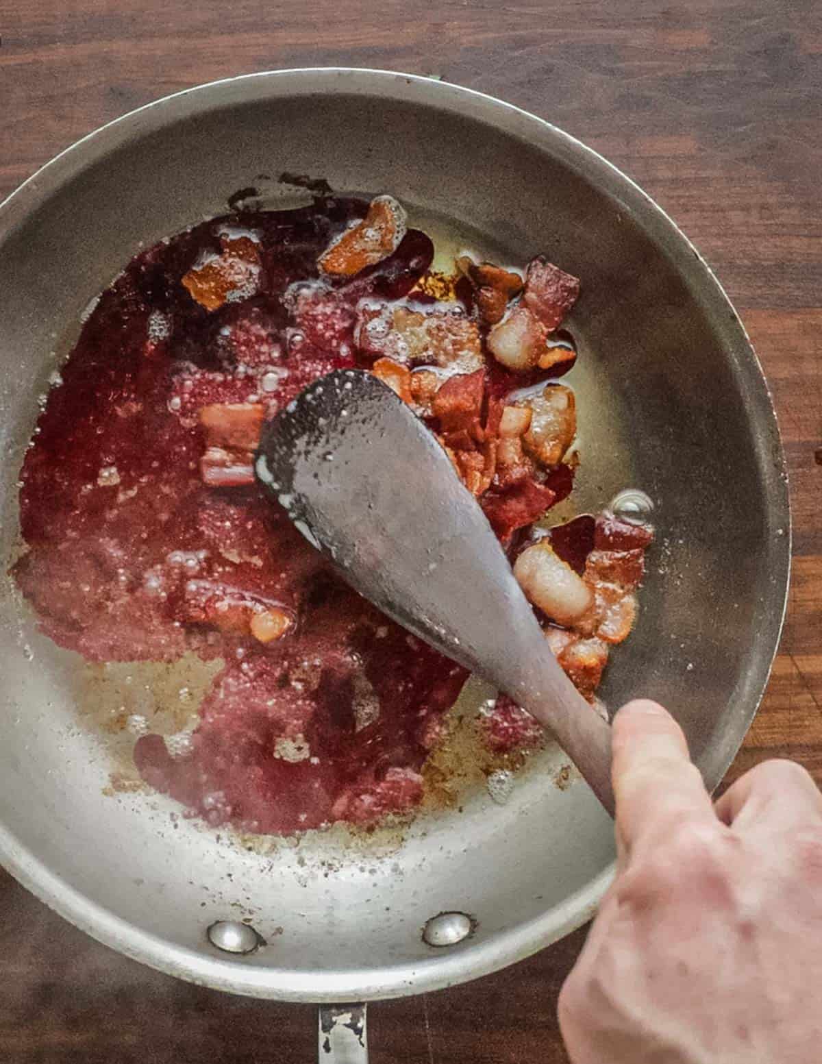 Scraping up the browned bits of bacon with a spoon. 