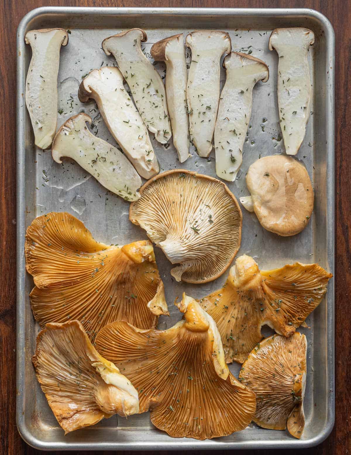 King oyster, fall oyster and blue oyster mushrooms seasoned with salt, oil and thyme on a baking sheet. 