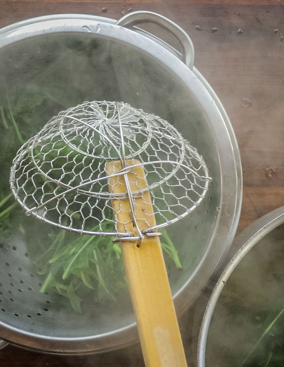 Removing cooked horta plants from a pot into a colander. 