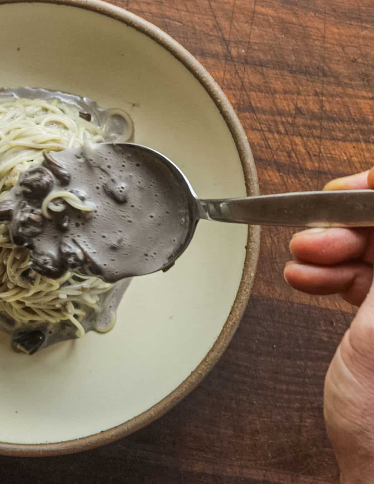 Spooning mushroom sauce over a finished bowl of capellini pasta. 