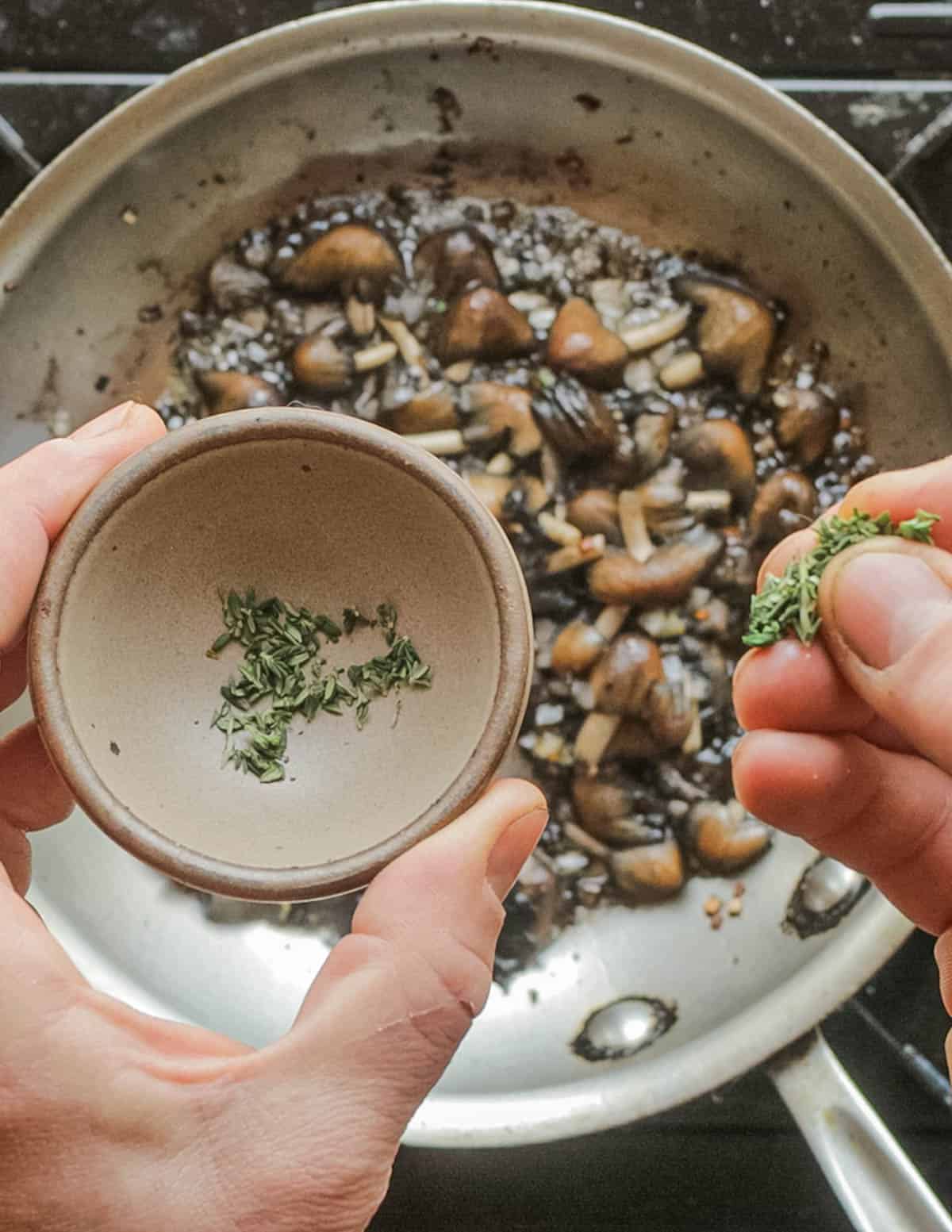 Adding fresh chopped thyme leaves to a pan of mushrooms cooking. 