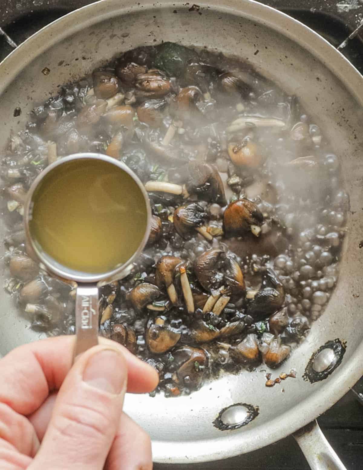Adding chicken stock to a pan with mushroom sauce.