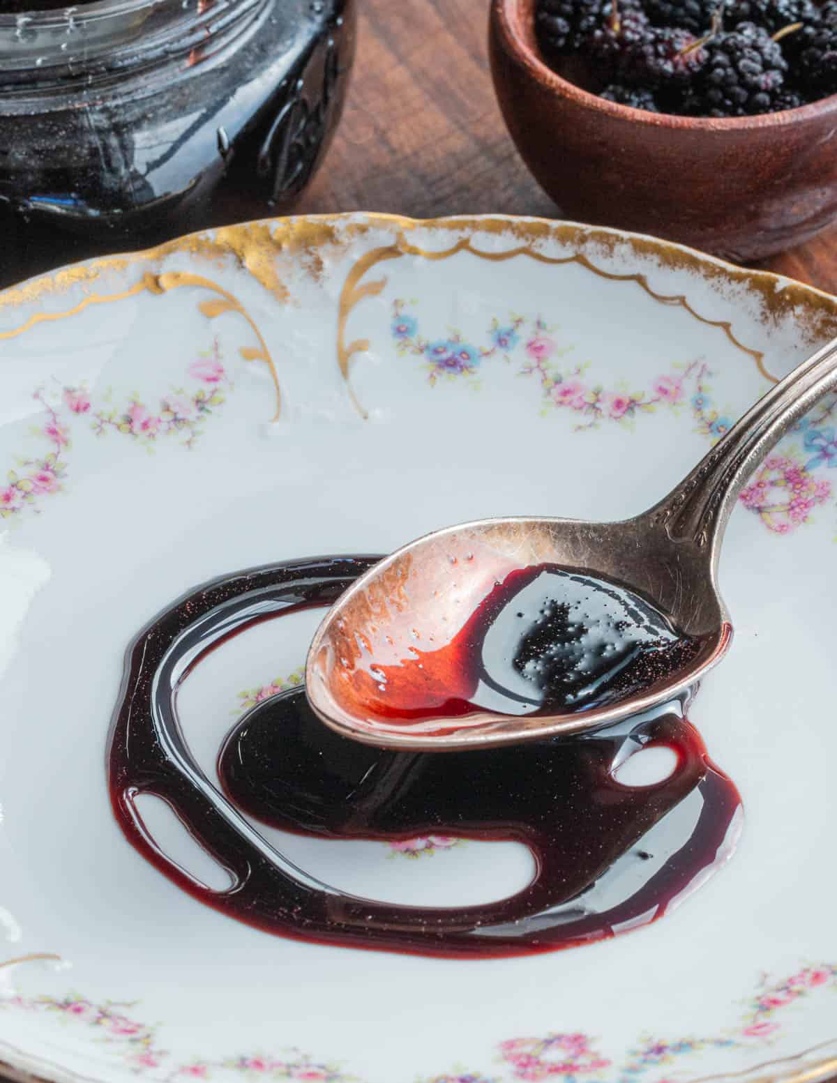 A spoon drizzling a black mulberry syrup on a plate. 