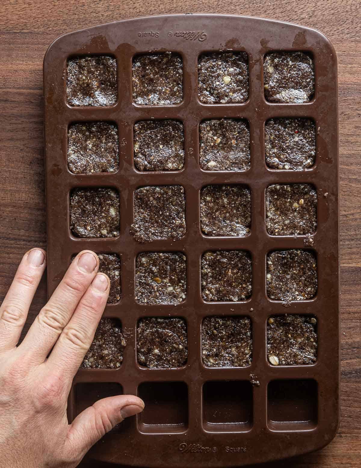 Pressing down black walnut cookie dough into a silicone baking mold. 