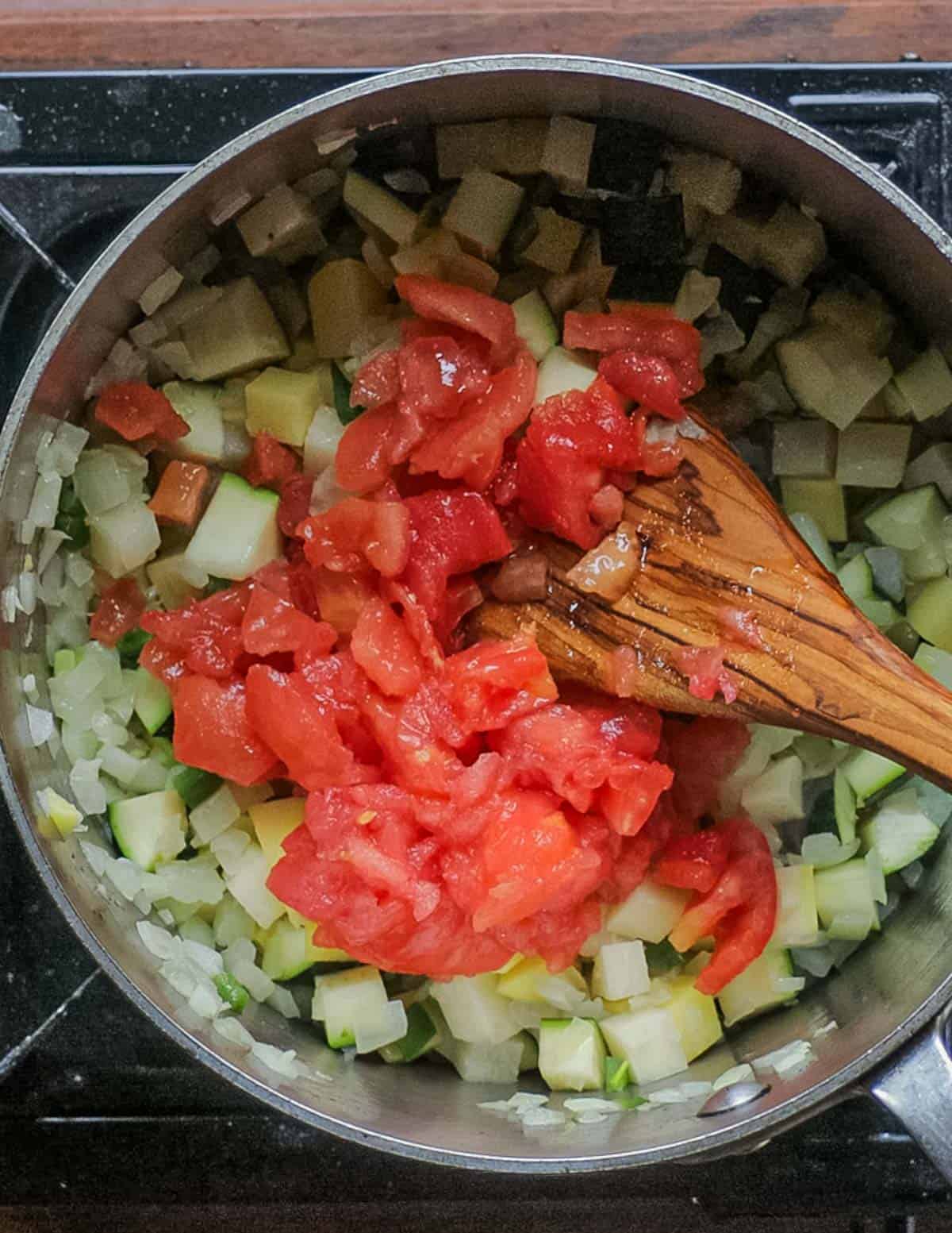 Adding chopped peeled tomatoes to a pot of soup. 