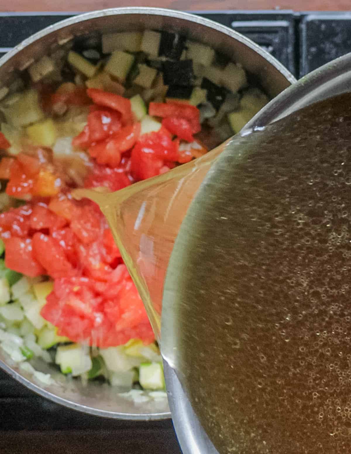 Pouring chicken stock into a pot of soup. 