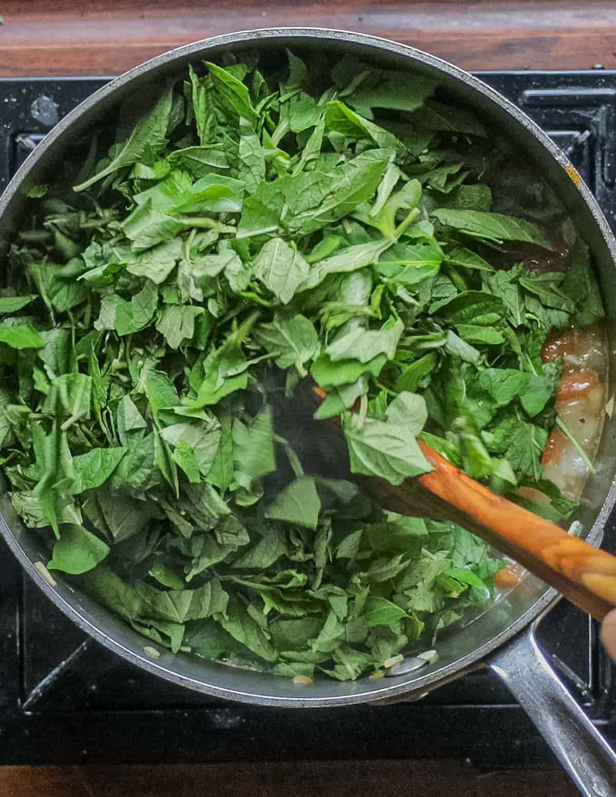 Adding sliced mora leaves or nightshade greens to a pot of soup. 