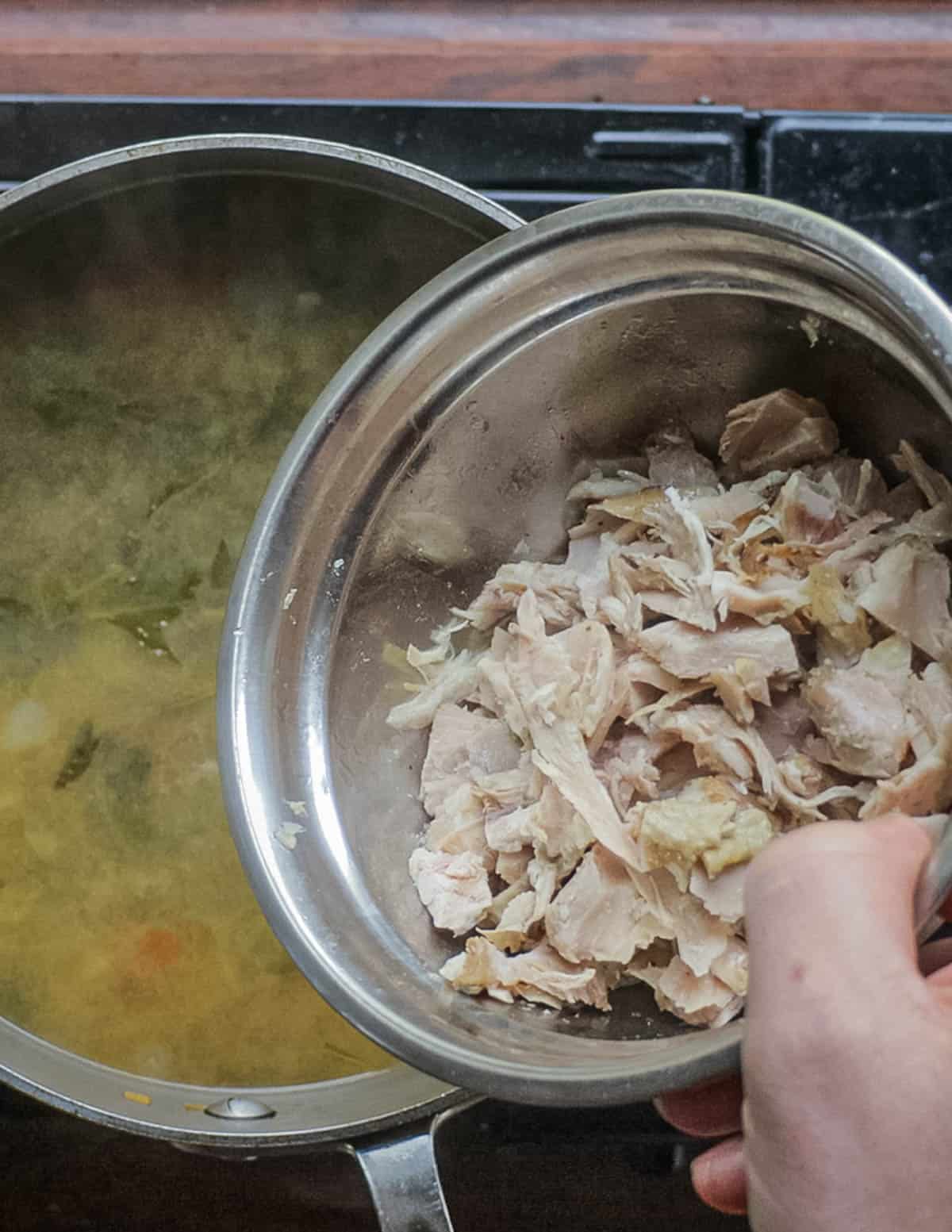 Adding cooked chicken to a pot of sopa de mora. 