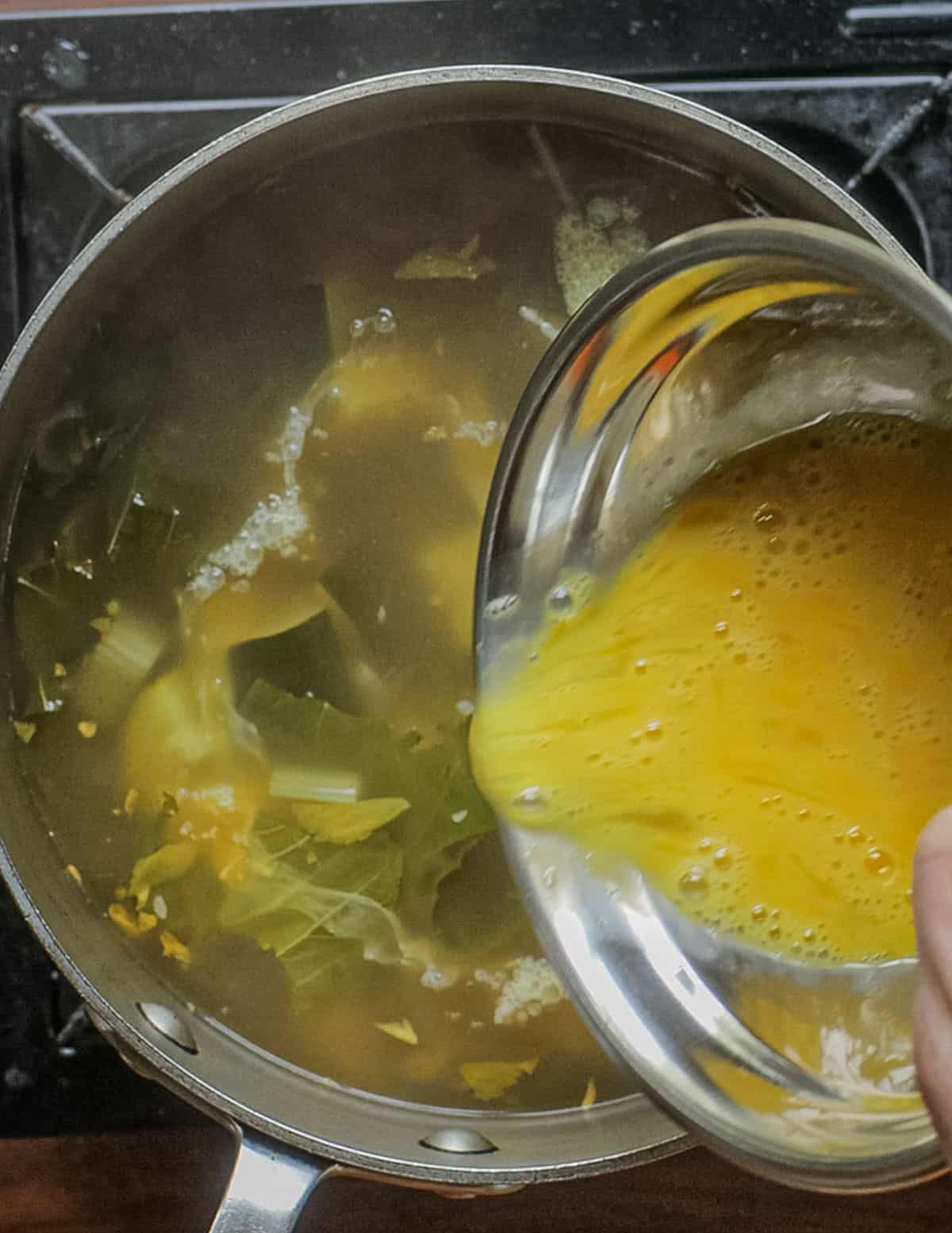 Adding beaten egg to a pot of mora soup to finish it. 