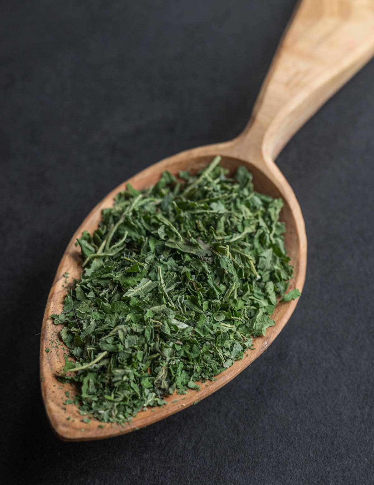 A close up image of dried nettle leaf tea on a hand carved spoon. 