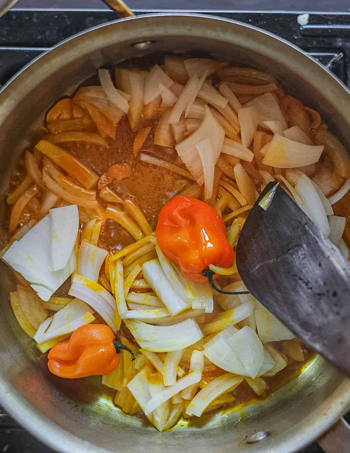 Cooking an onion and habanero peppers in red palm oil in a pot. 