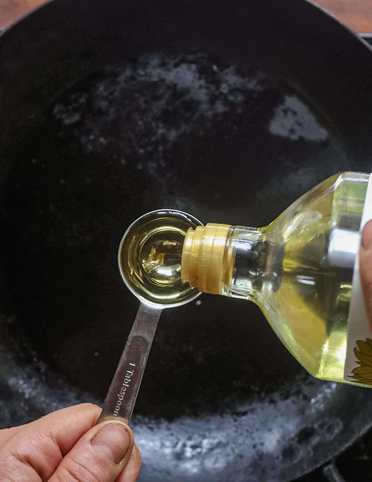 Pouring cooking olive oil into a carbon steel pan from the bottle. 