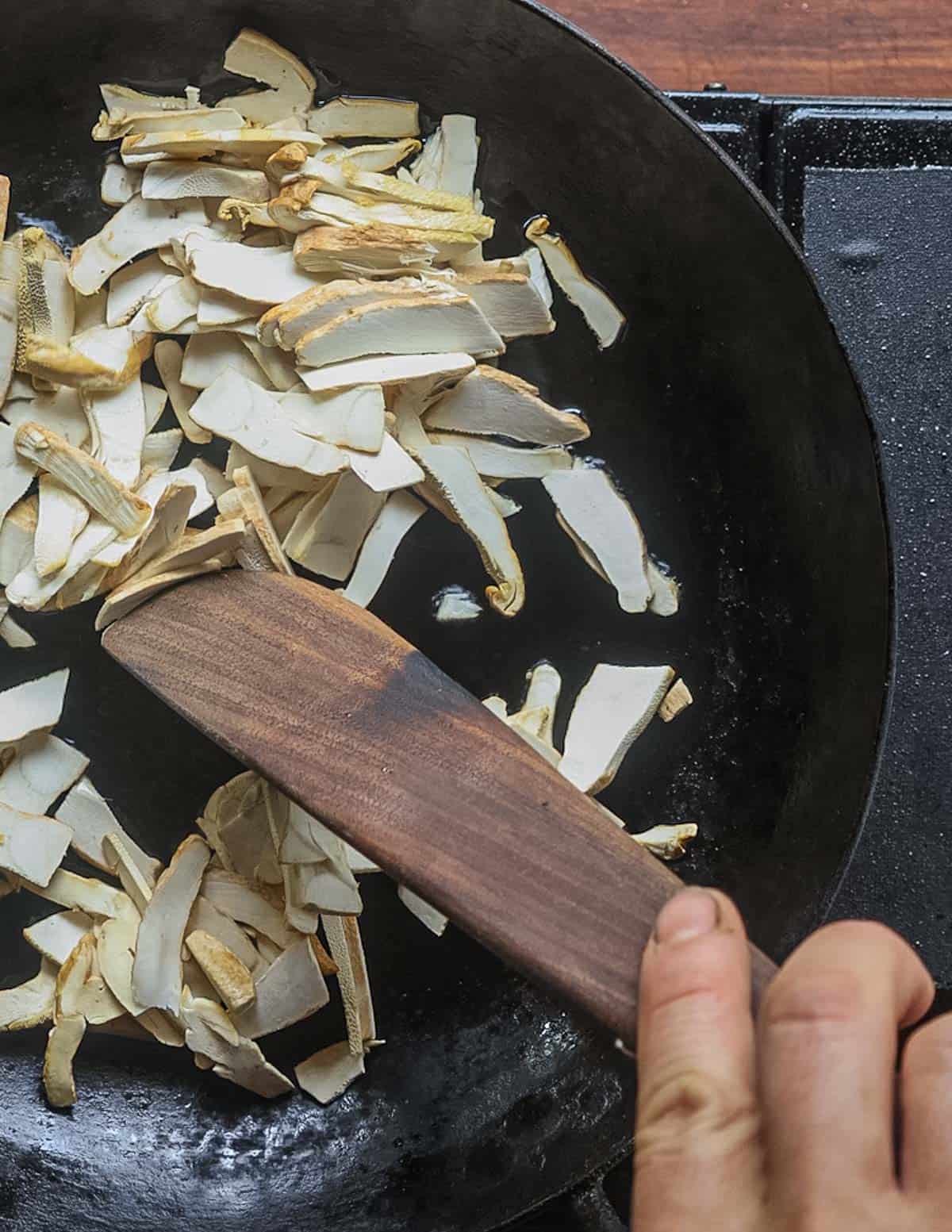 Stirring sliced polypore mushrooms with a wooden spoon. 